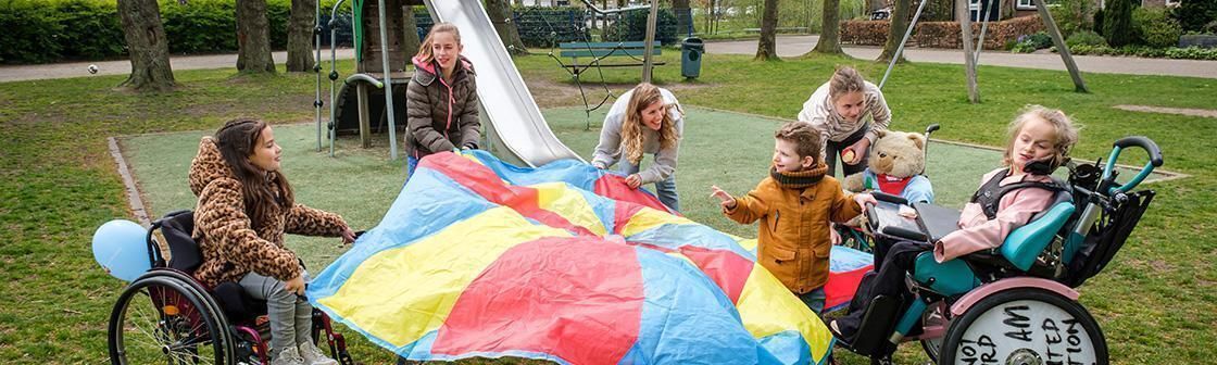 Kinderen met en zonder rolstoel spelen samen met een groot gekleurd zeildoek