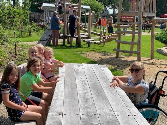 Meisje in rolstoel is aangeschoven aan de picknicktafel, samen met haar vriendjes