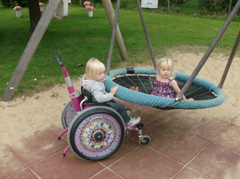 Meisje in rolstoel duwt een kleuter die in de nestschommel zit