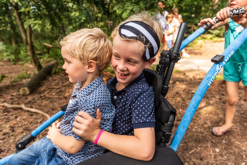 Twee kinderen in een speciale rolstoel worden voortgeduwd door het bos